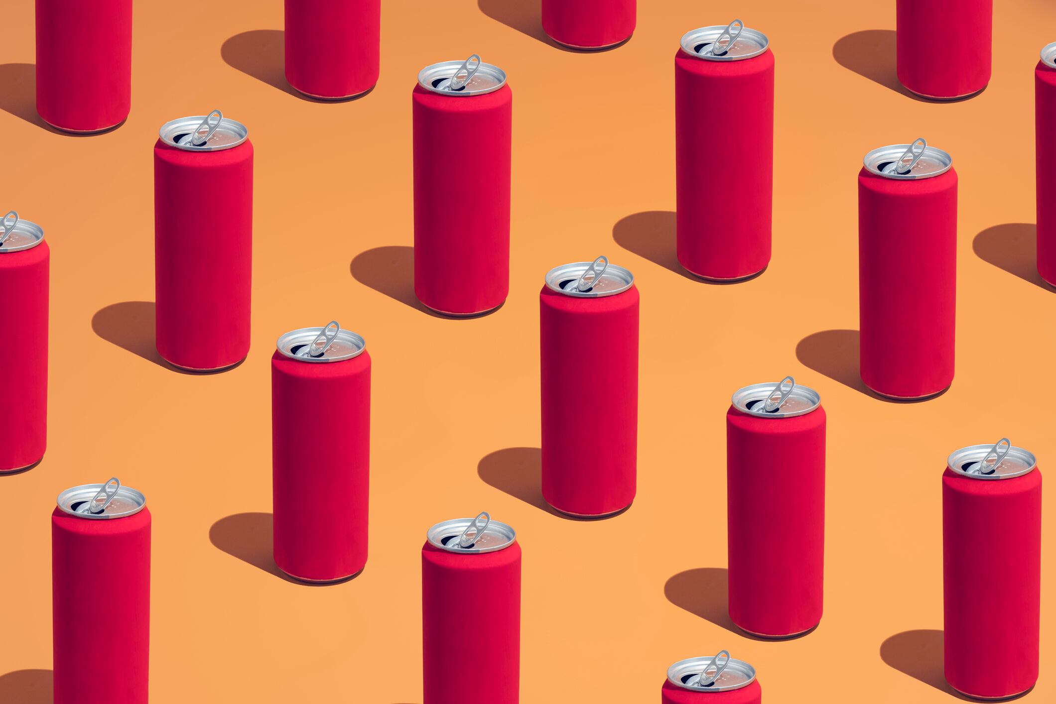 A group of red cola cans laid in a repetative pattern on a colorful background