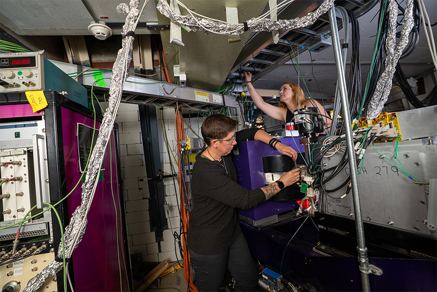 Two people work on FIONA. Cables wrapped in foil connect to the instruments and a panel of electronics.