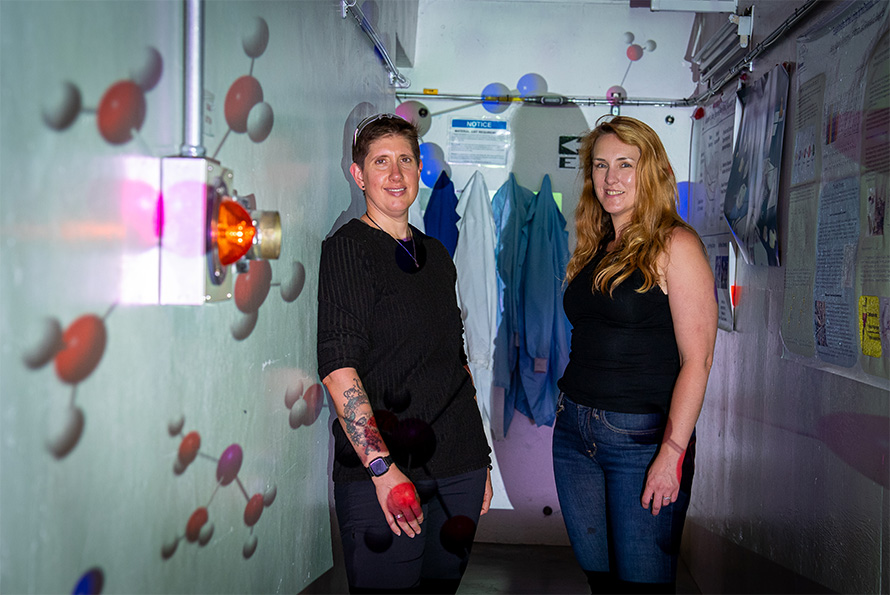 Red, blue, and white ball-and-stick models of molecules are projected onto two people in a hallway.