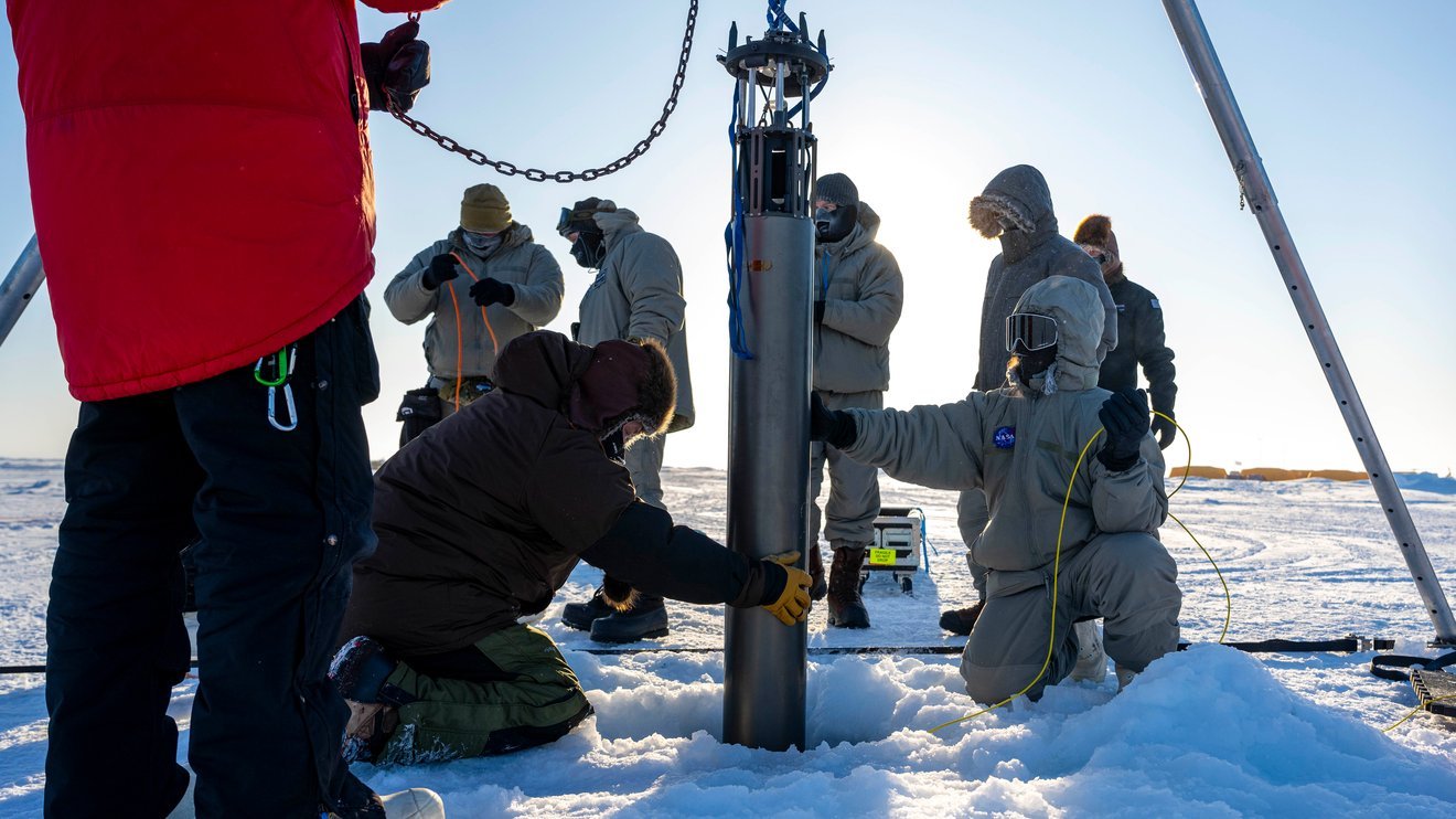 People in a snowy environment with a cylindrical instrument in the ground