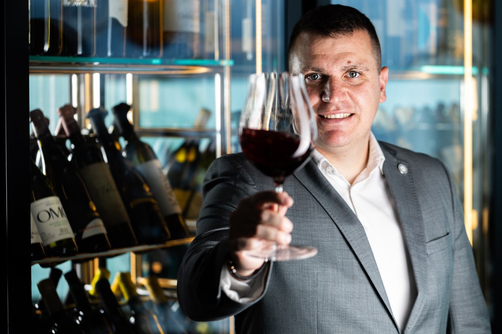 Sommelier Tomislav Mikinac at Nebo Restaurant & Lounge, Sommelier Tomislav Mikinac smiling holding glass of wine up with hand