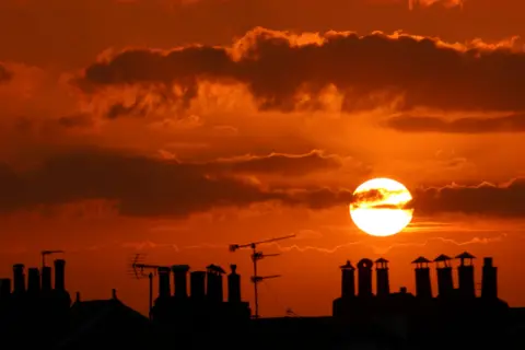 Marie-Pierre Garroway Vivid burnt orange sky with the sun setting above the silhouette of chimneys 