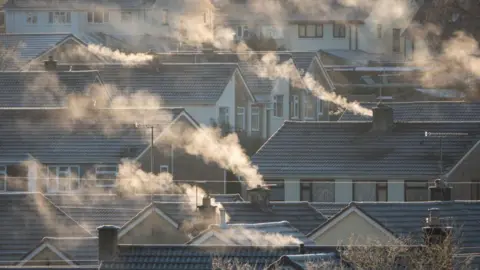 Getty Images Steam or smoke comes from chimneys on roofs of a number of houses on a frosty day.