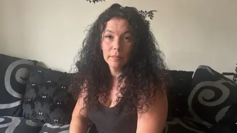 A woman with long dark curly hair sitting on a black and grey patterned sofa