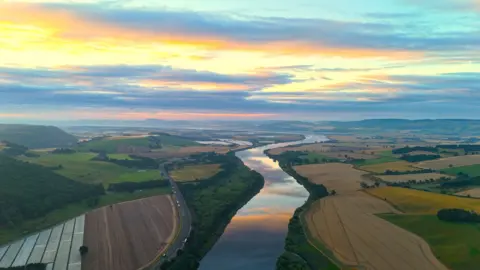 Kevin Hamill Aerial view of the River Tay, winding between fields on both sides below a vivid blue, yellow, orange and pink sky at sunrise 