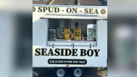 Supplied Max Linduschka and Bradley Gibbs are standing in a white food van which has Spud-on-Sea and Seaside Boy written on the front. They are both standing inside wearing yellow and black T-shirts.