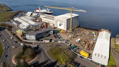 Aerial shot of a shipyard with a large ship at the quay and a large, yellow crane among numerous buildings