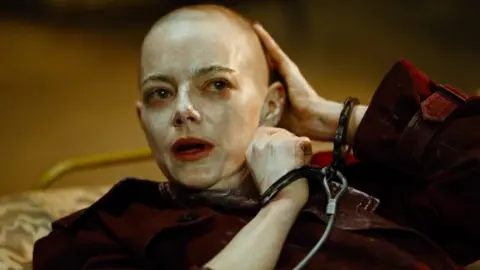 Universal Emma Stone as seen in Bugonia, with a shaved head and in handcuffs