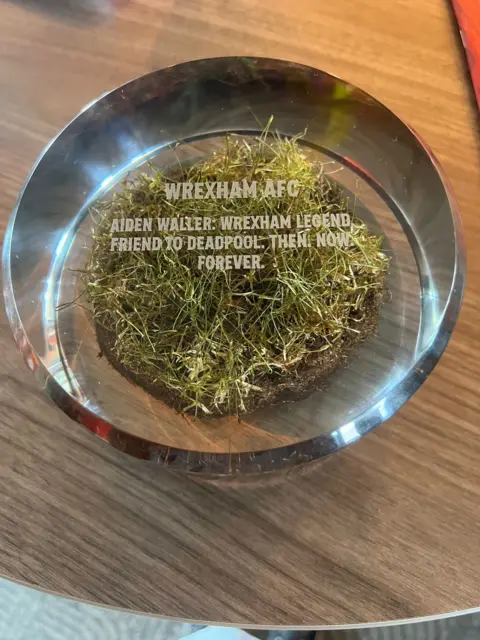 Sarah Waller The circular turf glass plaque, which reads: "Wrexham AFC: Aiden Walker. Wrexham Legend. Friend to Deadpool. Then. Now. Forever."