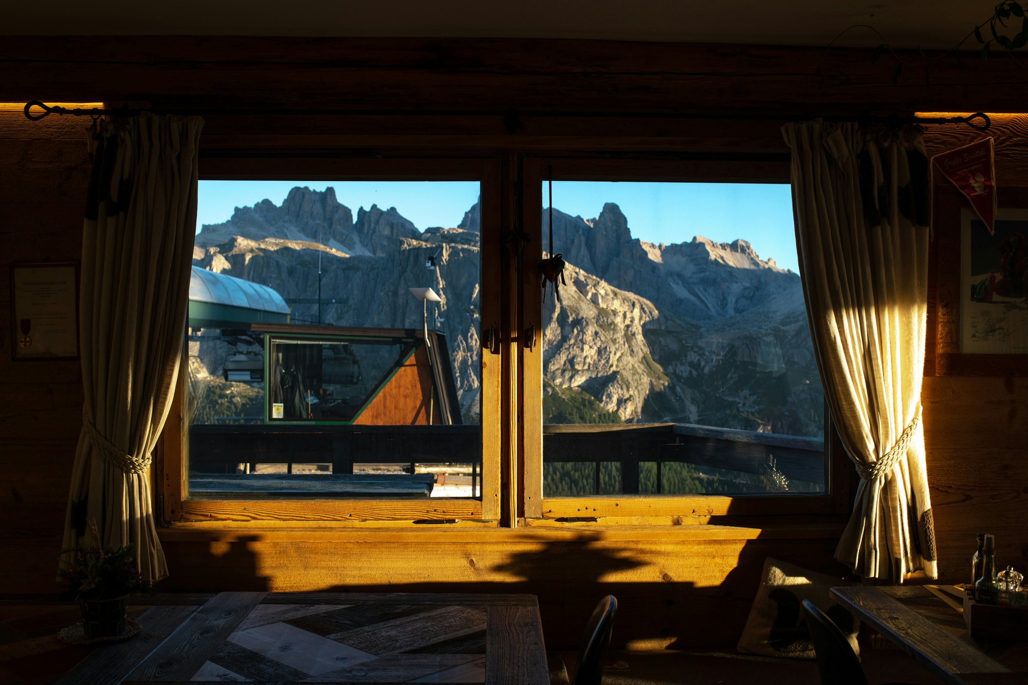The view of mountains through a window in a cabin, framed by curtains.