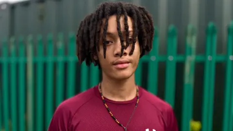Martin Giles A boy with a purple top and a green metal fence in the background