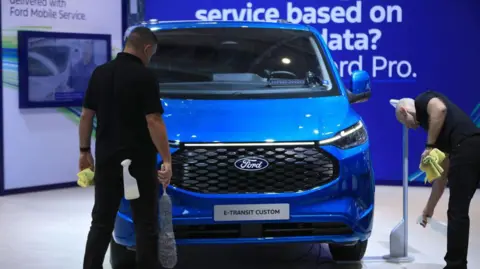 Bloomberg via Getty Images Employees prepare a a bright blue Ford E-Transit Custom electric van for display at the IAA Transportation commercial vehicle fair in Hannover, Germany, on Monday, 16 September 2024. 