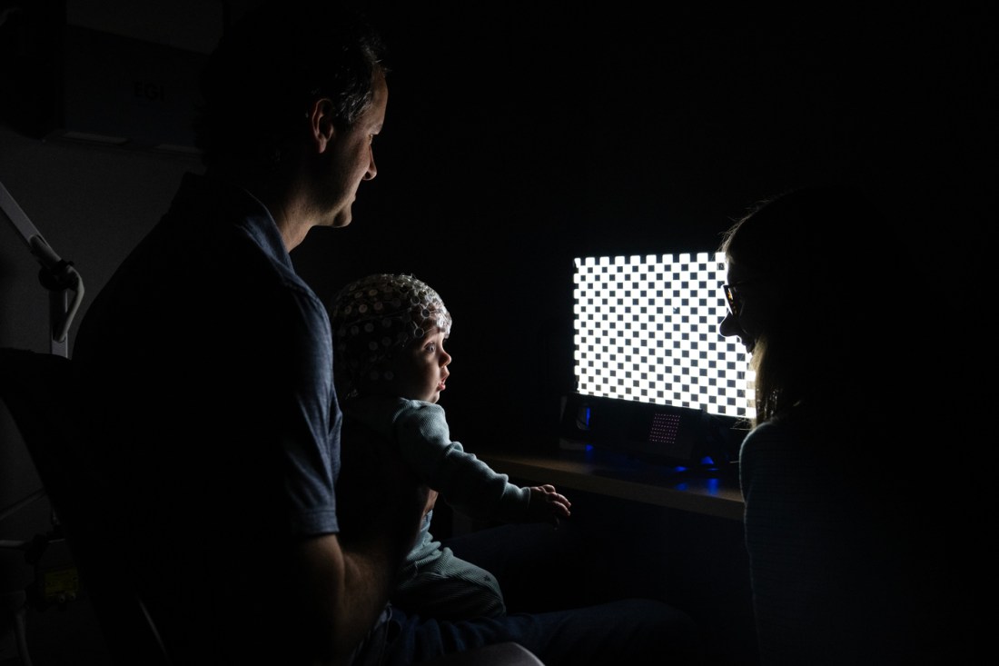 Two adults in the lab with a newborn baby, positioned in front of a rectangular white light.