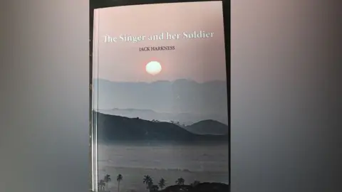 contributed/Alamy A photo of the front cover of the book. It says The Singer and Her Soldier in white font with the name JACK HARKNESS in black capitals below that. The photo shows sunset over a tropical sea, with palm trees in the foreground and hills and mountains behind the waves. A pale pink sky with a glowing sun is at the top.