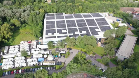 Bottle Yard Studios A view of The Bottle Yard Studios site from the air. It shows solar panels on the roof, trees, shrubbery and parked cars.