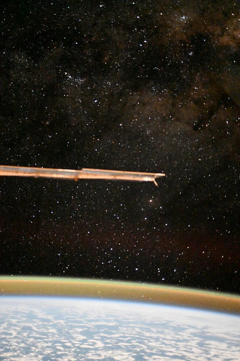 a solar array extends into the frame from the left, perforating a view of the starry sky and Earth's horizon as seen from a space station