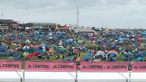 David Dixon/BBC A sloping field is covered with spherical and triangular tents in multi-colours.