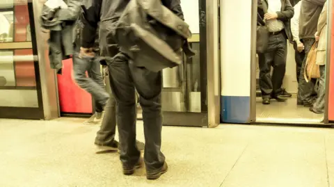Getty Images People crowd into a London tube carriage, as a person on the platform starts to board. The image only shows the people from below the neck.