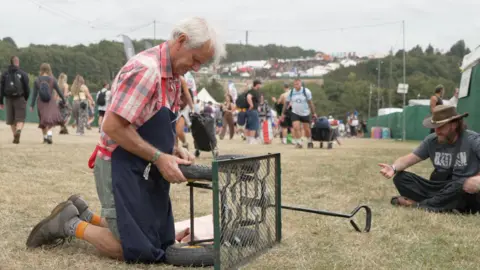 Charles Cole fixing a trolley at the festival. He is on his knees, stuffing the wheel with fabric.