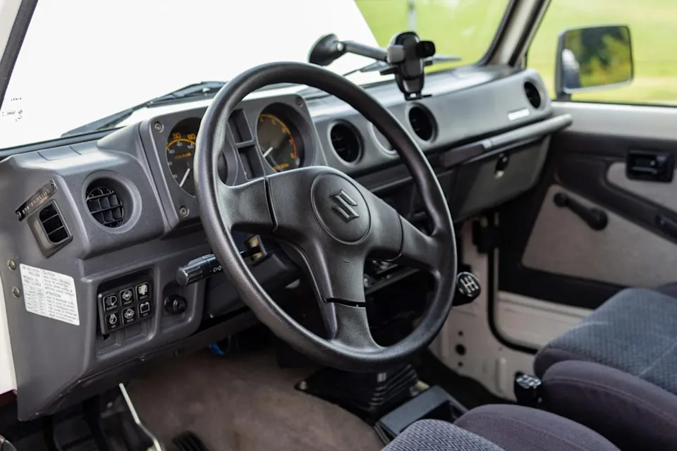 interior view from driver side seat showing three spoke steering wheel, analog gauges, and manual gear shifter.