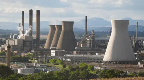 PA Media A view of the Grangemouth petrochemical plant in Grangemouth. A large white tower is in the foreground, with three darker ones further away. Smoke billows from the chimneys f various buildings in the heavily industrial site