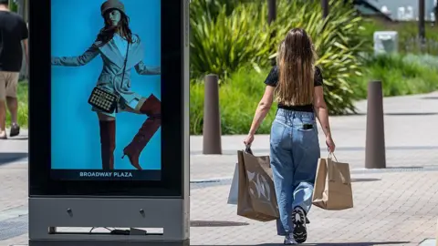 Bloomberg/Getty A female shopper with long brown hair at the Broadway Plaza Shopping Center in Walnut Creek, California, walking on the sidewalk carrying shopping bags