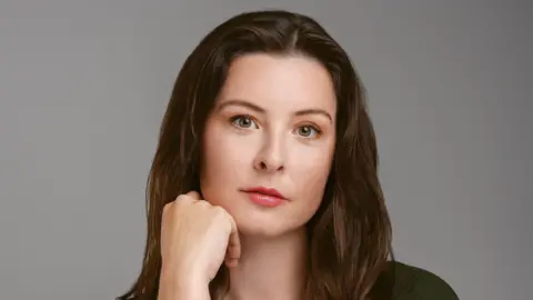 Alexa Morden Alexa Morden, a woman with long brown hair, wearing glossy lipstick, looking into the camera with one hand resting on her chin