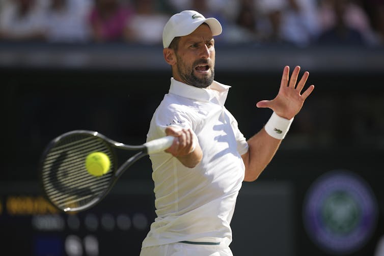 A tennis player wearing all white hits a forehand