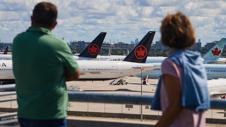 Two people look out over a balcony at planes sitting on the runway at an airport