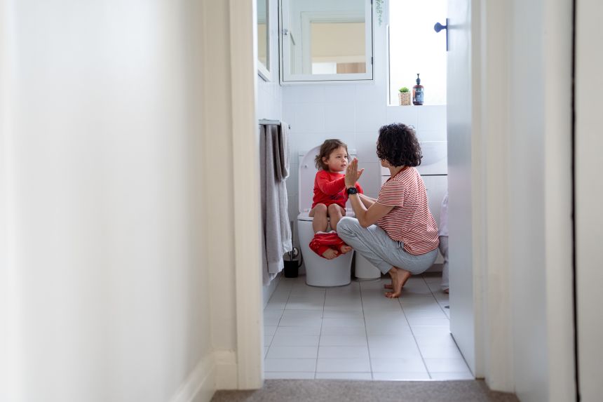 A young girl potty training with her parent.
