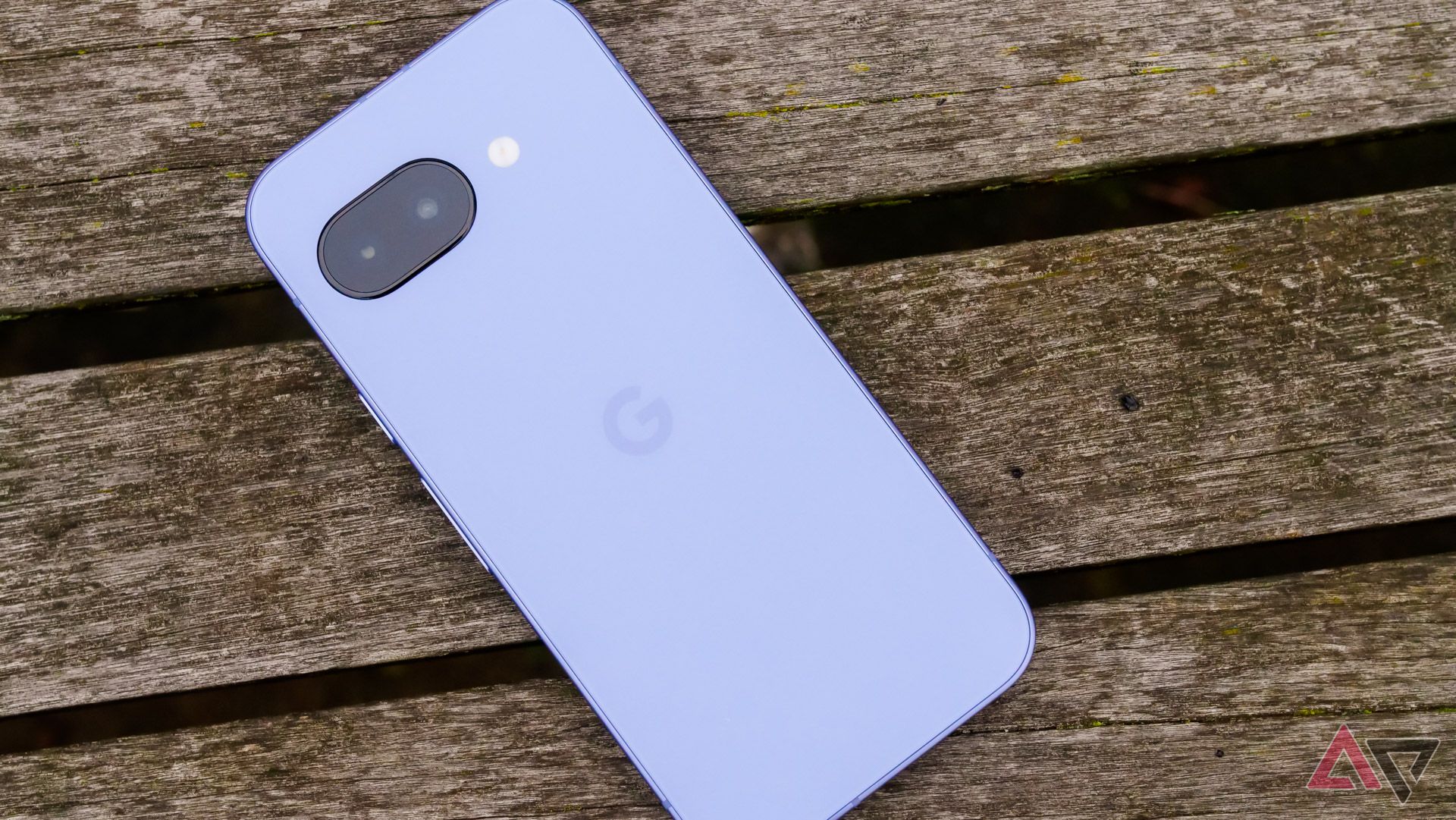 The Google Pixel 9a on a wooden bench in a park, face down.