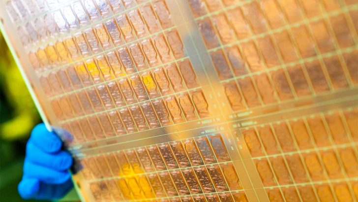 Gloved hand holding a semiconductor wafer with intricate circuit patterns.