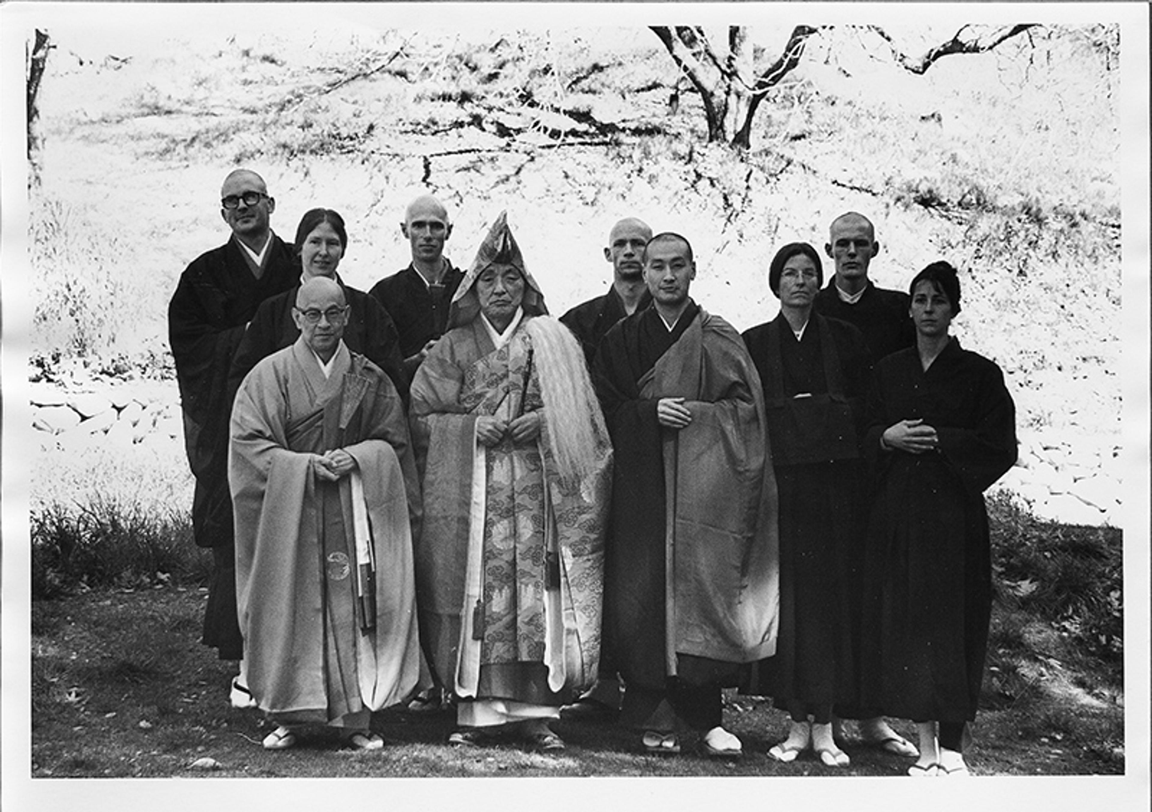 Black and white photo of a group of Buddhist monks and nuns in traditional robes standing outdoors.