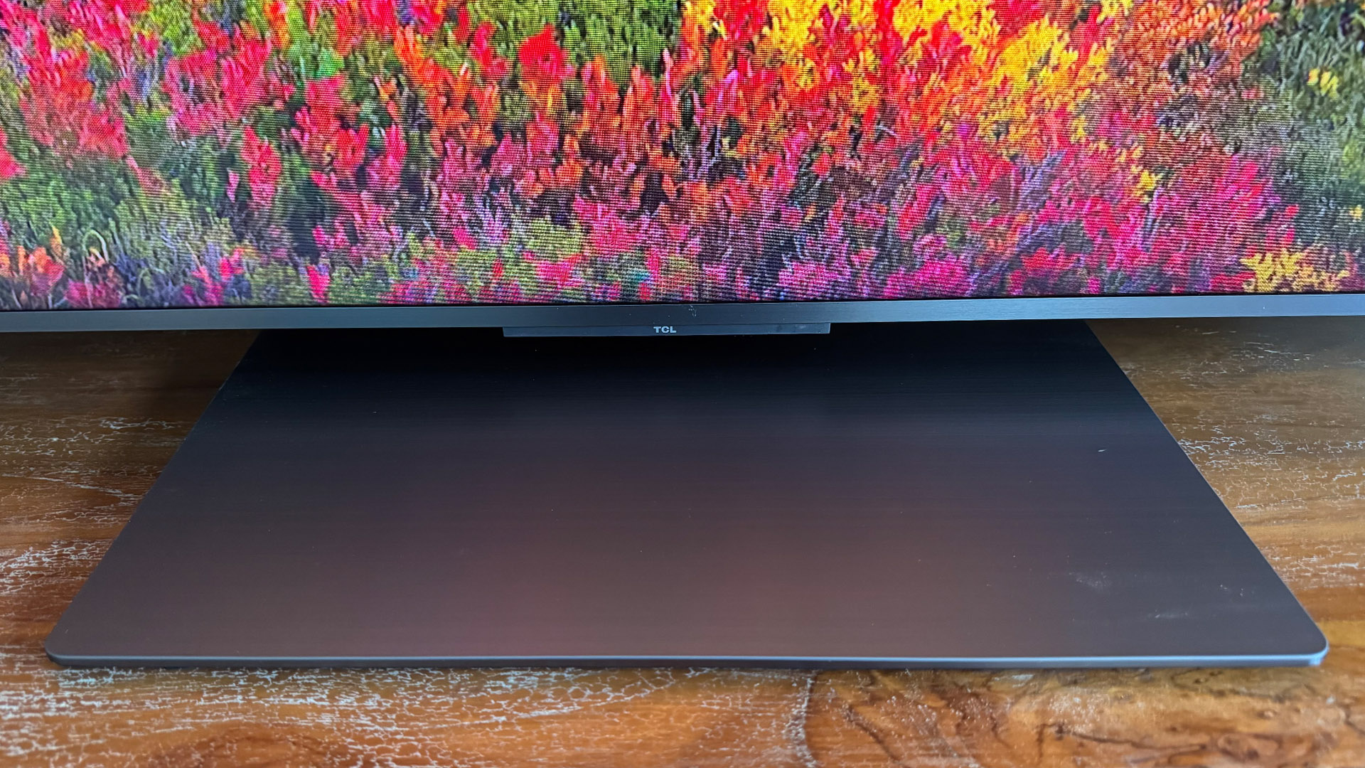 TCL 65C8K LCD TV close up on. bottom of TV and stand, on screen is image of flowers