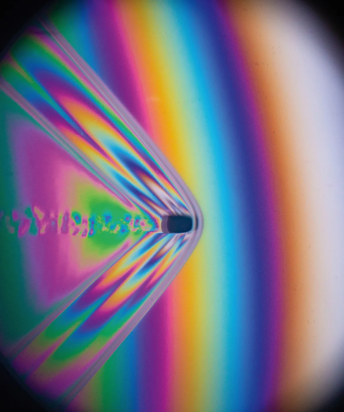A .22 caliber bullet fired from a rifle flies through the air. This image uses polarizing interferometry to show difference in air pressure, represented by different colors of light. The clear bow wave in front of the bullet shows that it is moving faster than the speed of sound. The exact velocity of this supersonic bullet can be calculated from measurements of the bow wake angle. This image freezes the motion by using a high speed flash with a duration of 1/2,000,000th of a second.