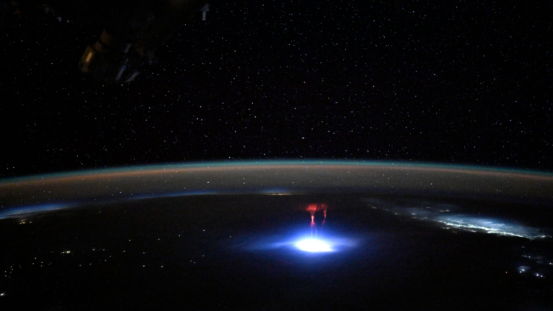 a bright red jet of light climbs into Earth's upper atmosphere atop a large bright white flash of lightning.