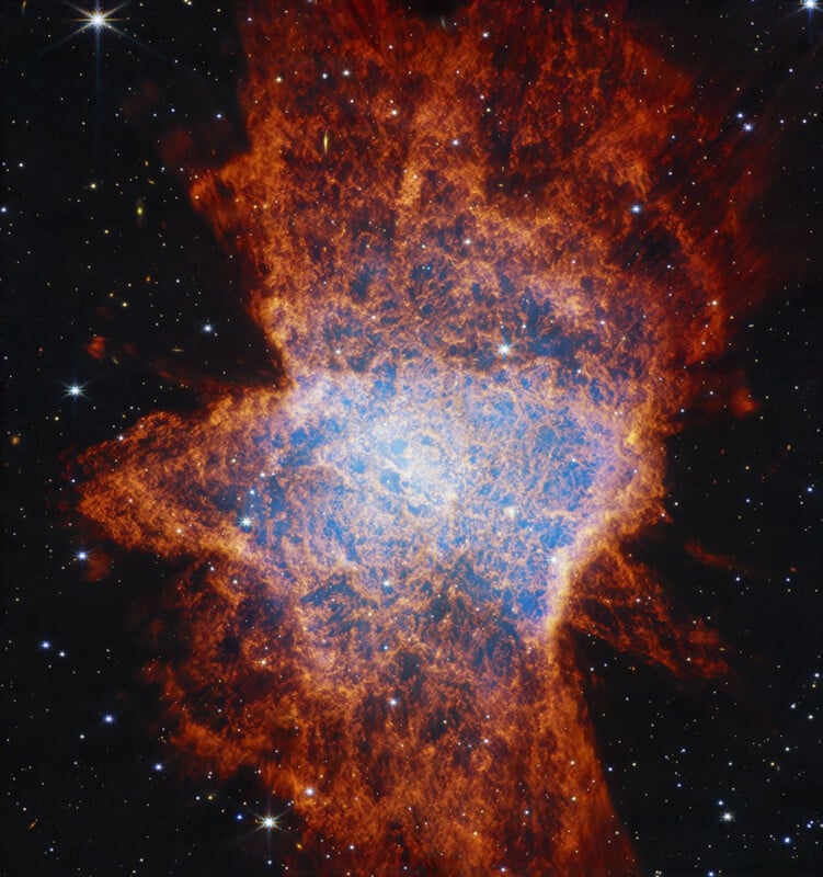 A vivid image of a nebula in space, showing a bright blue core surrounded by intricate, fiery red and orange clouds, with numerous stars scattered in the dark background.
