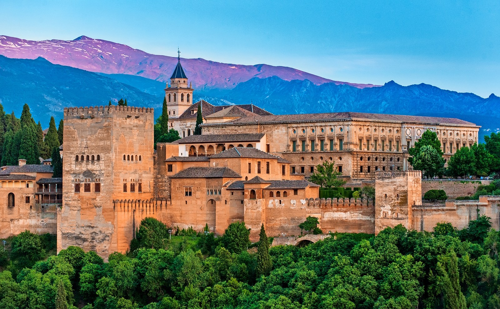The Alhambra, a fortress and palace complex in Granada, Spain, with mountains in the background.