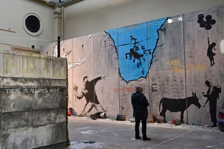 A man looks at British street artist Banksy's mural "The Bethlehem Wall" during a preview of the exhibition "The world of Banksy, the immersive experience" at the Milano Centrale main railway station in Milan on December 02, 2021. [Miguel Medina/AFP]