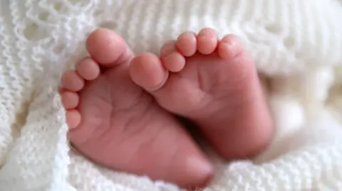 PA Media A new born baby's feet peeking out of a shawl