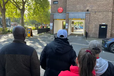 The back of the heads of four residents facing a brick building