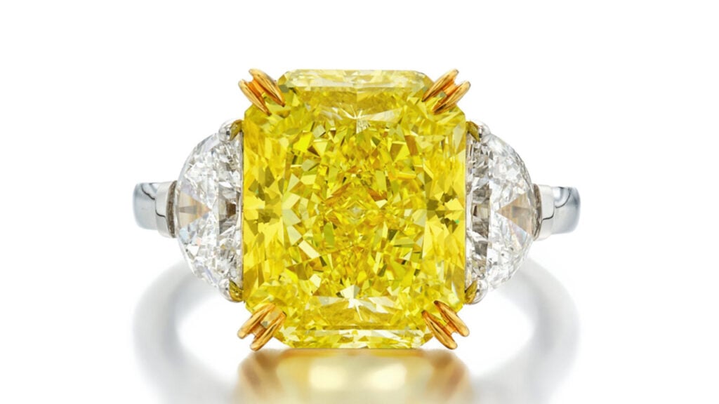 A ring features a cut-cornered rectangular modified brilliant-cut, 6.82-carat, fancy-vivid-yellow diamond between a pair of half-moon diamonds by Sotheby's image