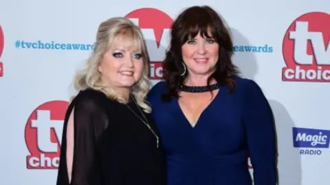 PA Media Linda Nolan, wearing a black dress and on crutches, with her sister Coleen, who had on a drak blue dress, at a TV awards do at The Dorchester Hotel in London in 2017.