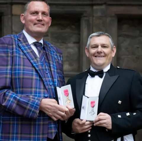 Getty Images A photo of John and Doddie with their MBEs outside the palace