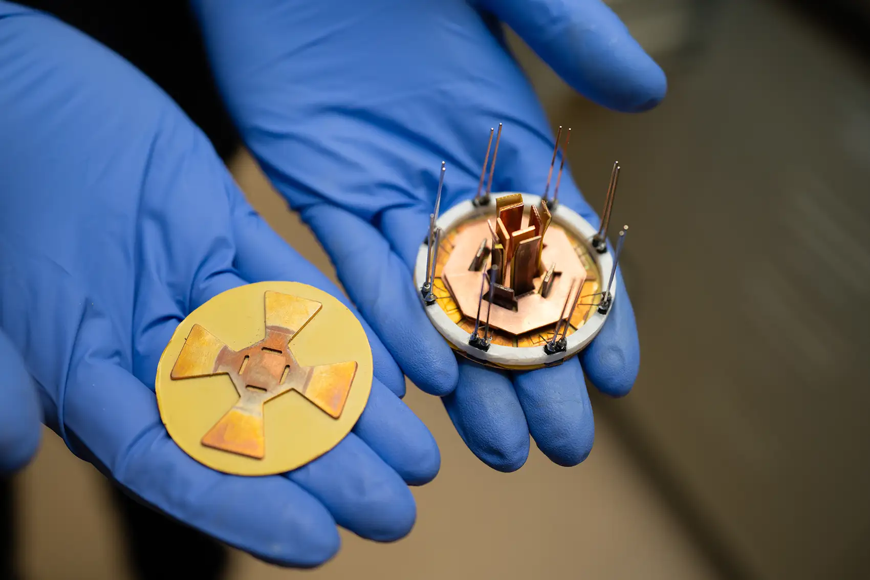 Two gloved hands hold a small octagonal power module and a corresponding attachment layer.