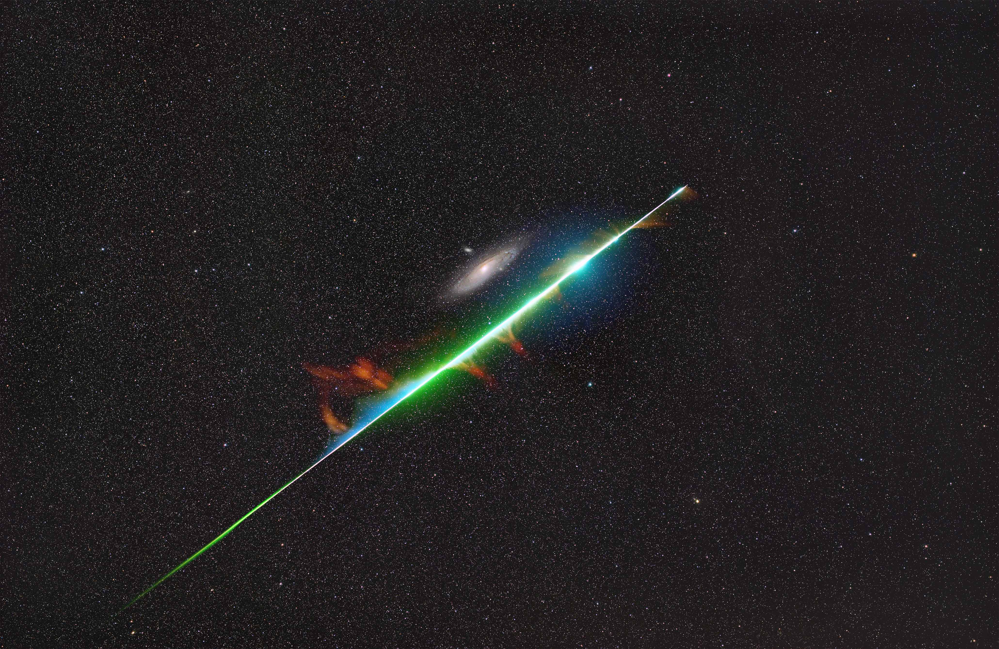 A bright meteor is pictured streaking through the sky next to the Andromeda spiral galaxy.