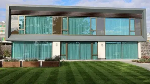 Betsi Cadwaladr health board The new Maggie's centre in north Wales. It has a glass frontage and a well-kept lawn and gardens to the front. It sits on the site of Ysbyty Glan Clwyd, which can be seen in the background.