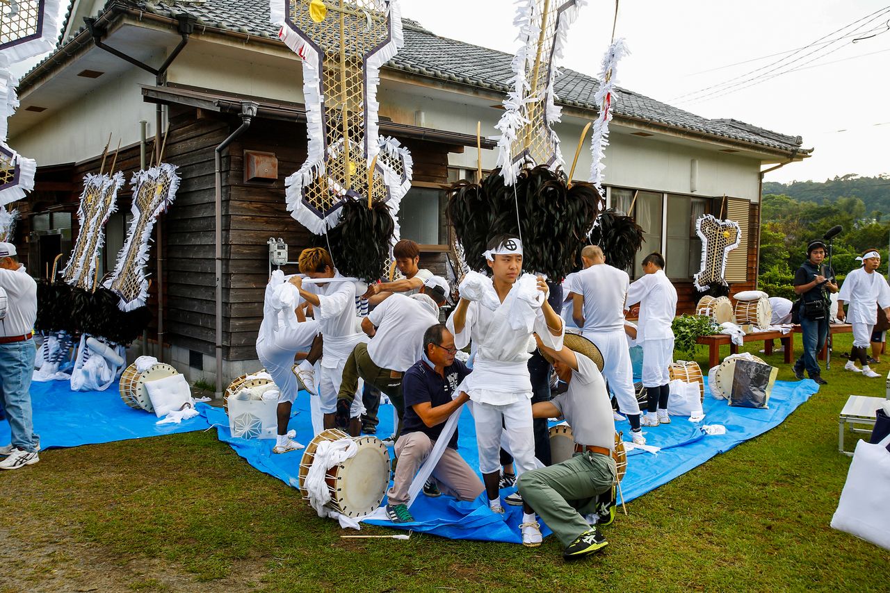 Assistants help the drummers into their costumes. (© Haga Library)