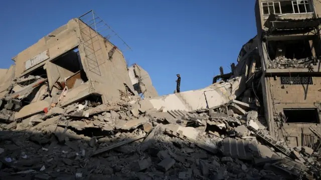 A Palestinian stands at the site of a collapsed residential building hit in an overnight Israeli airstrike, in Gaza City