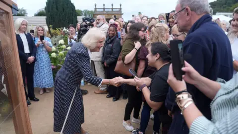 PA Media Queen Camilla meeting members of the public attending a showing of Pride and Prejudice on the lawns of Chatsworth House during The Queen's Reading Room Festival at Chatsworth House. She is shaking a woman's hand.